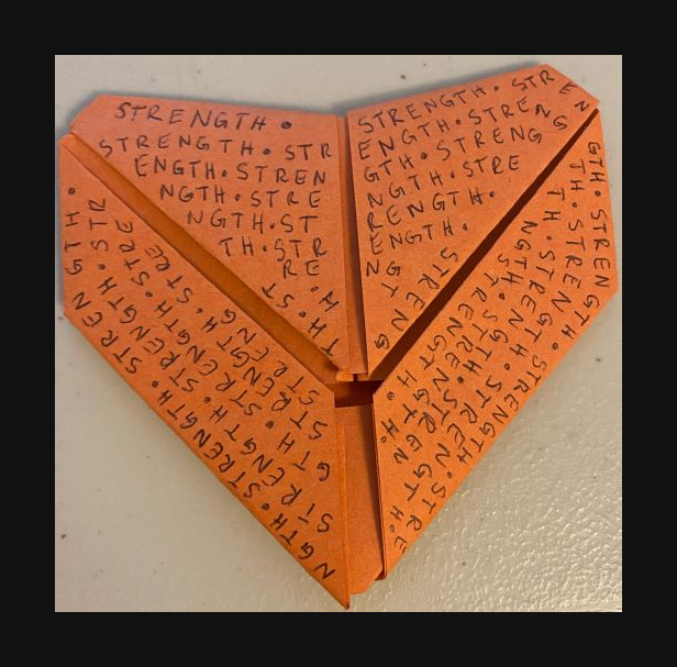 Origami heart with "strength" written in a pattern all over the paper